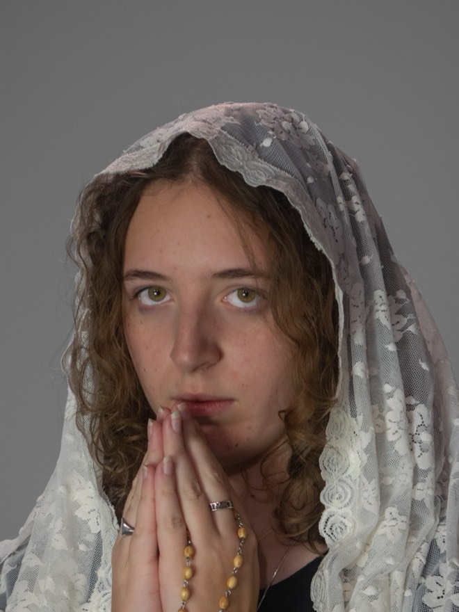 Mallory in a lace chapel veil, hands folded in prayer with a rosary