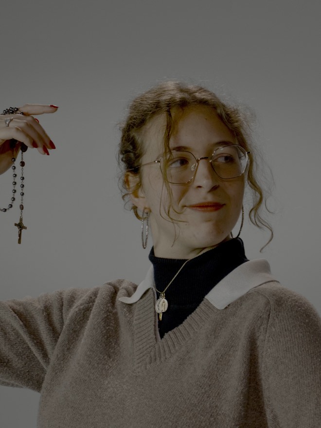 Mallory holding up a rosary with a wry sideways look